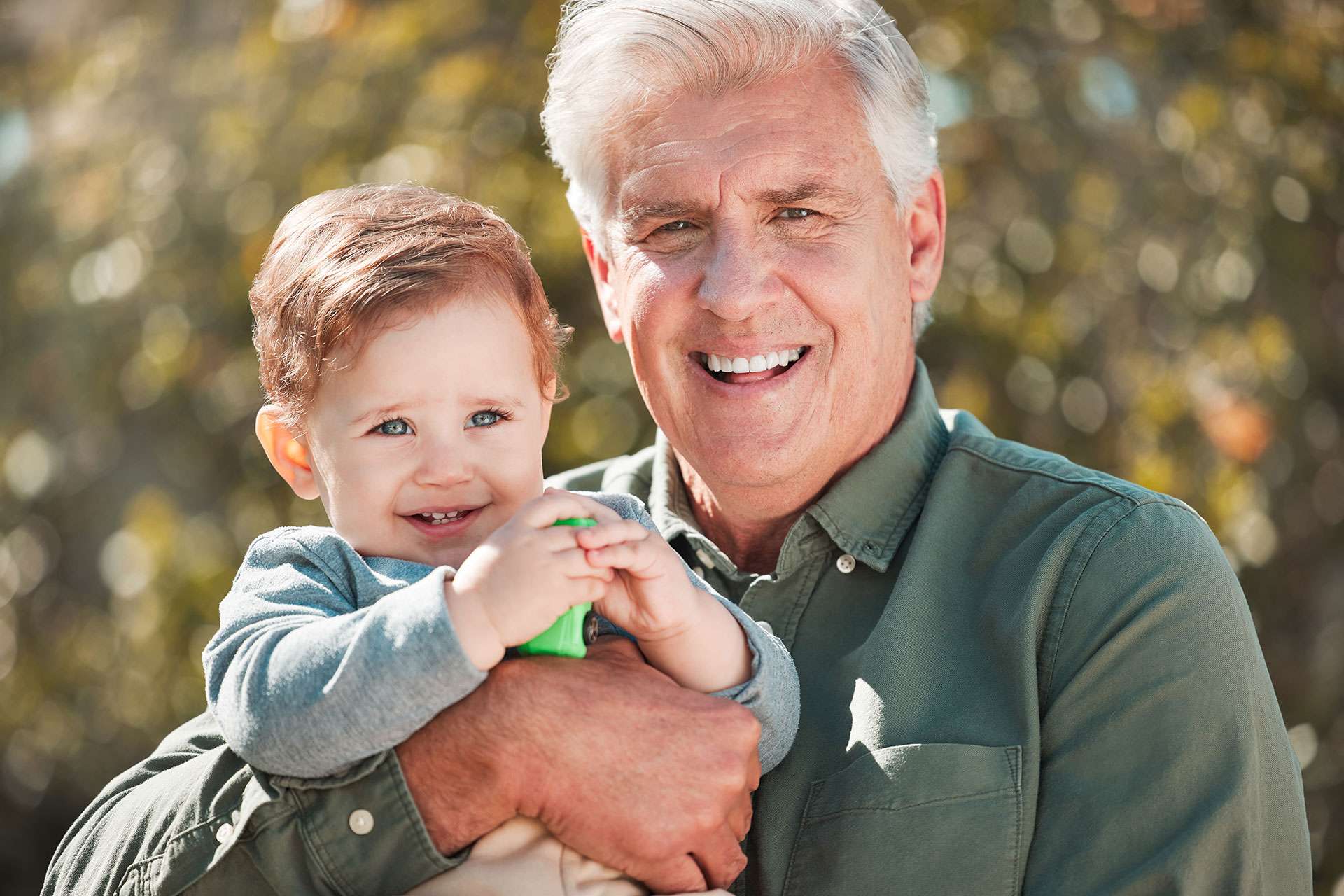 Grandfather holding smiling baby outdoors.